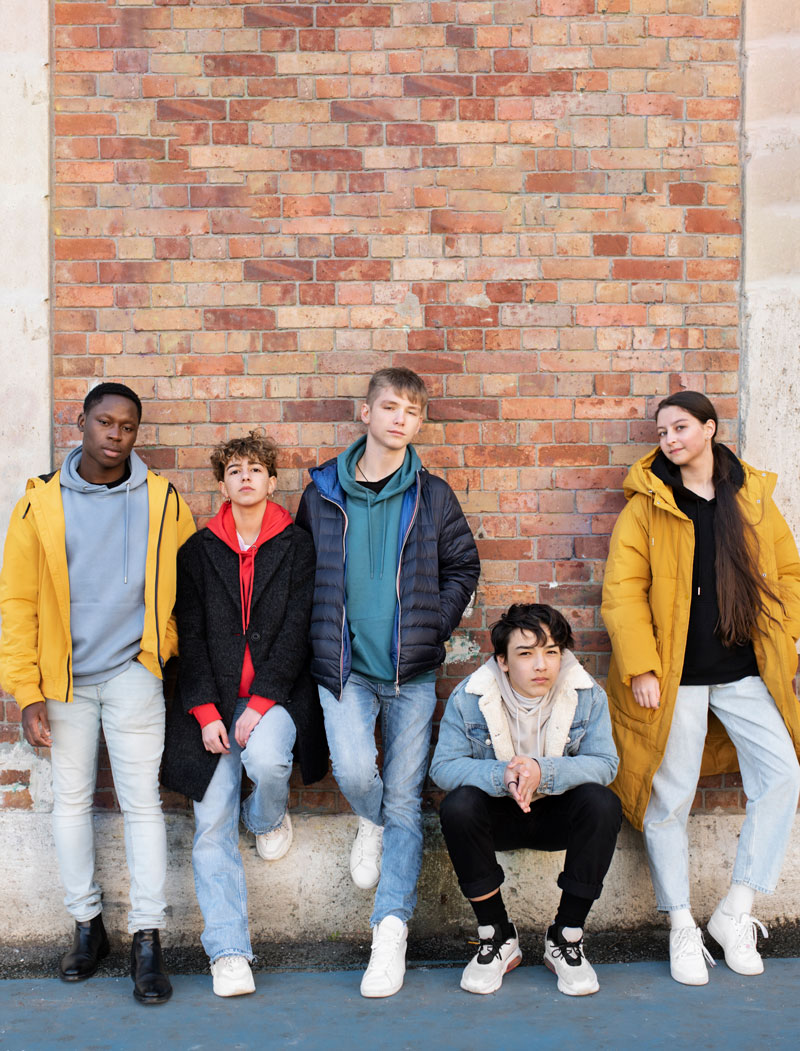 group of diverse teenagers standing against a wall spending time together