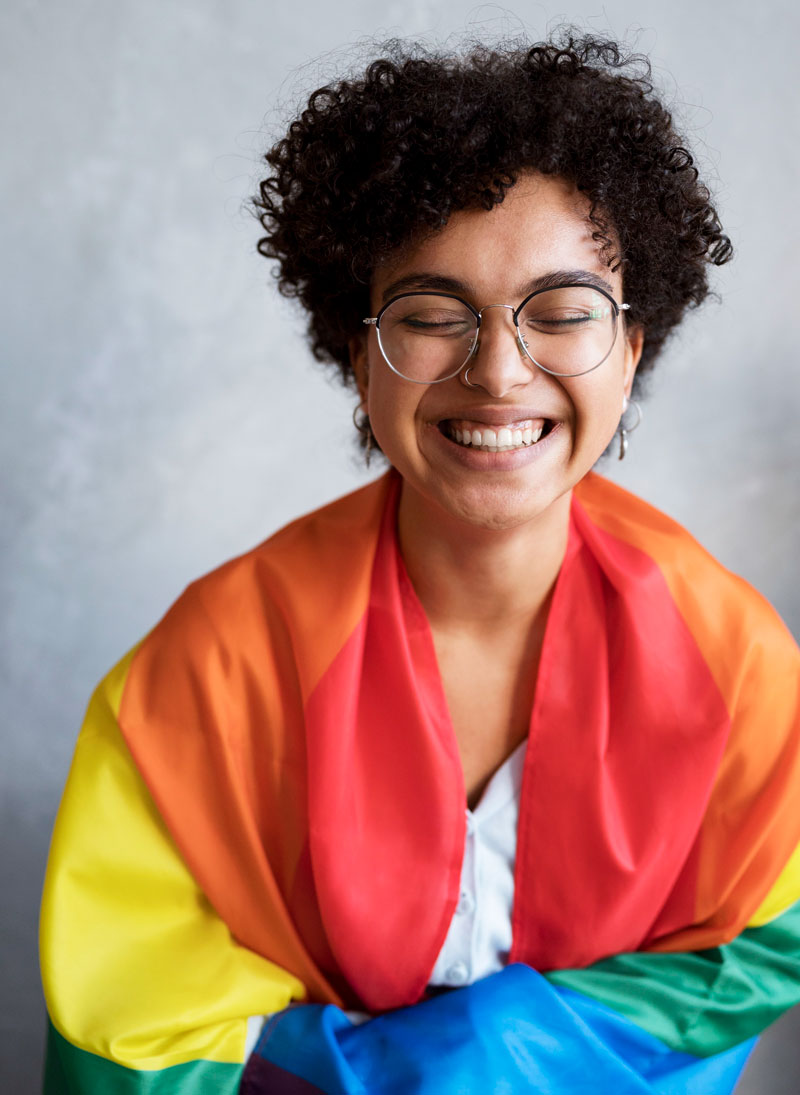 young smiling african american woman wearing an lgbtq flag around her shoulders