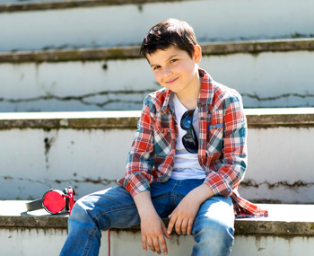 A teen boy sits down on some steps outdoors. Wondering if Therapy for Teens in Arlington, MA can help your teen? Speak with a teen therapist in MA to see how trauma in teens is affecting your teen.
