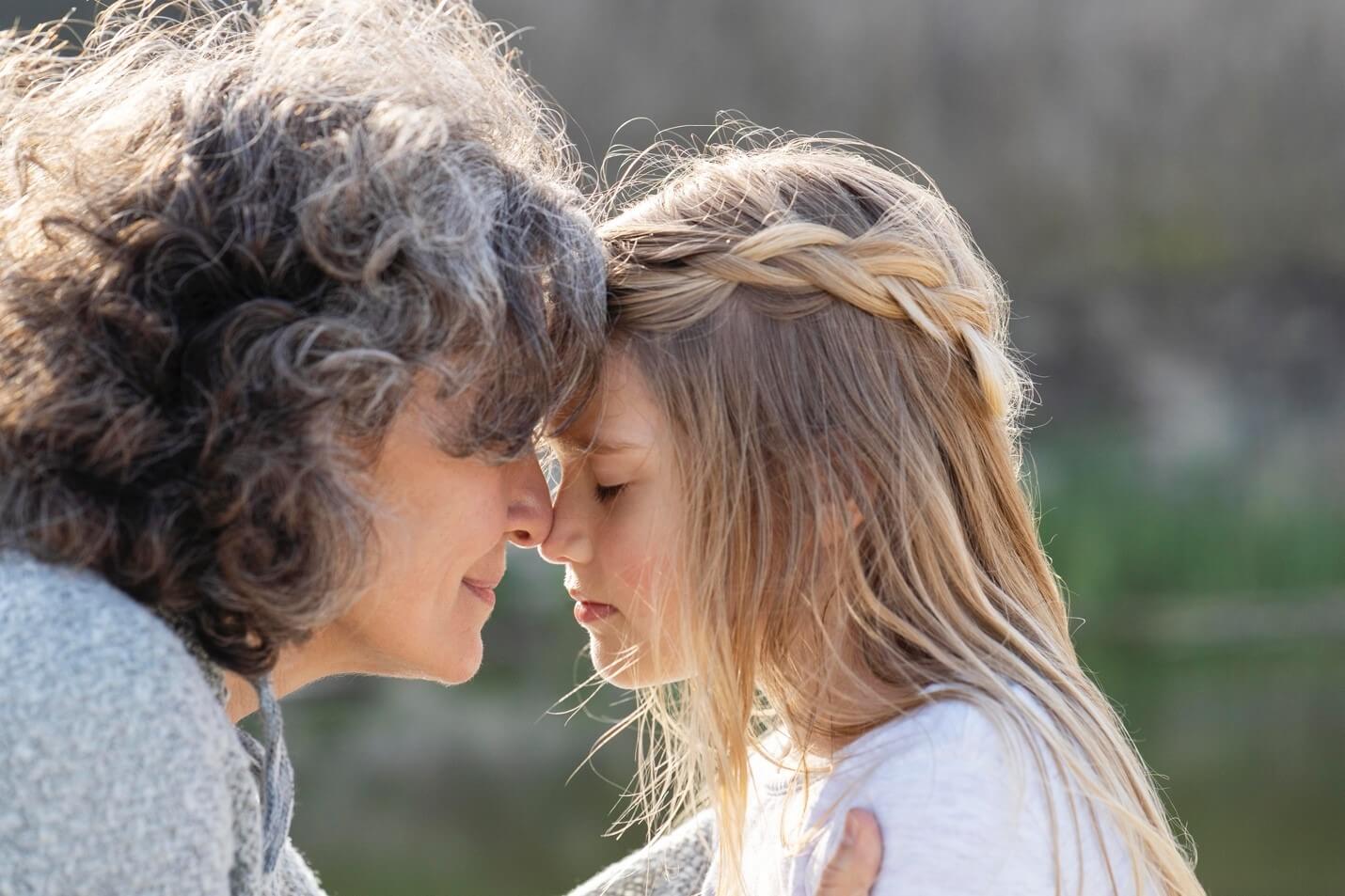 An older woman rests her head on her girl's head. Having a hard time as Anxious Parents in Arlington, MA? Speak with a therapist to see how they can provide parenting support through Therapy for Teens in Arlington, MA