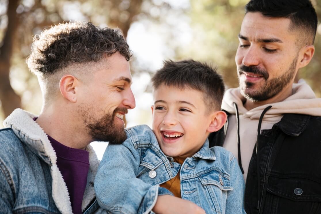Two men are smiling while holding their child. See how Therapy for teens in MA can provide the parental support you need as anxious parents in Arlington, MA. Speak with a therapist today to learn more!