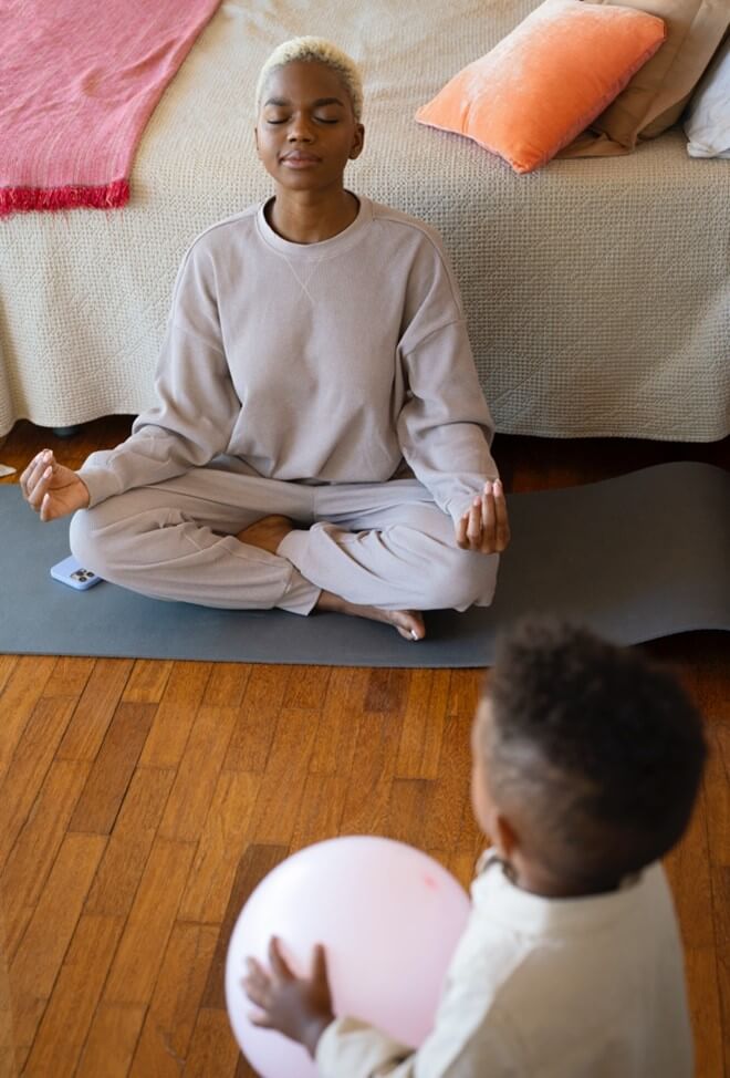 A woman sits on her floor doing yoga in front of a child. Struggling as Anxious Parents in Arlington, MA? Get Parenting Support through Therapy for Teens in Arlington, MA today!