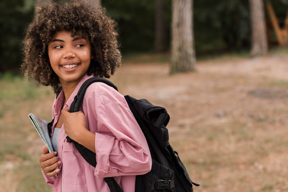 A teen with a backpack on stands in a grassy area near trees. Want to learn how CBT works for teens with autism in Arlington, MA? Speak with a teen therapist in MA to see how therapy for teens can help them.