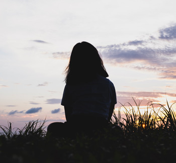 A silhouetted teen girl sits on a rock with the sunsetting. Wondering how to help your teens with depression in Arlington, MA? Speak with a teen therapist to see how Therapy for Teens in Arlington, MA can help.