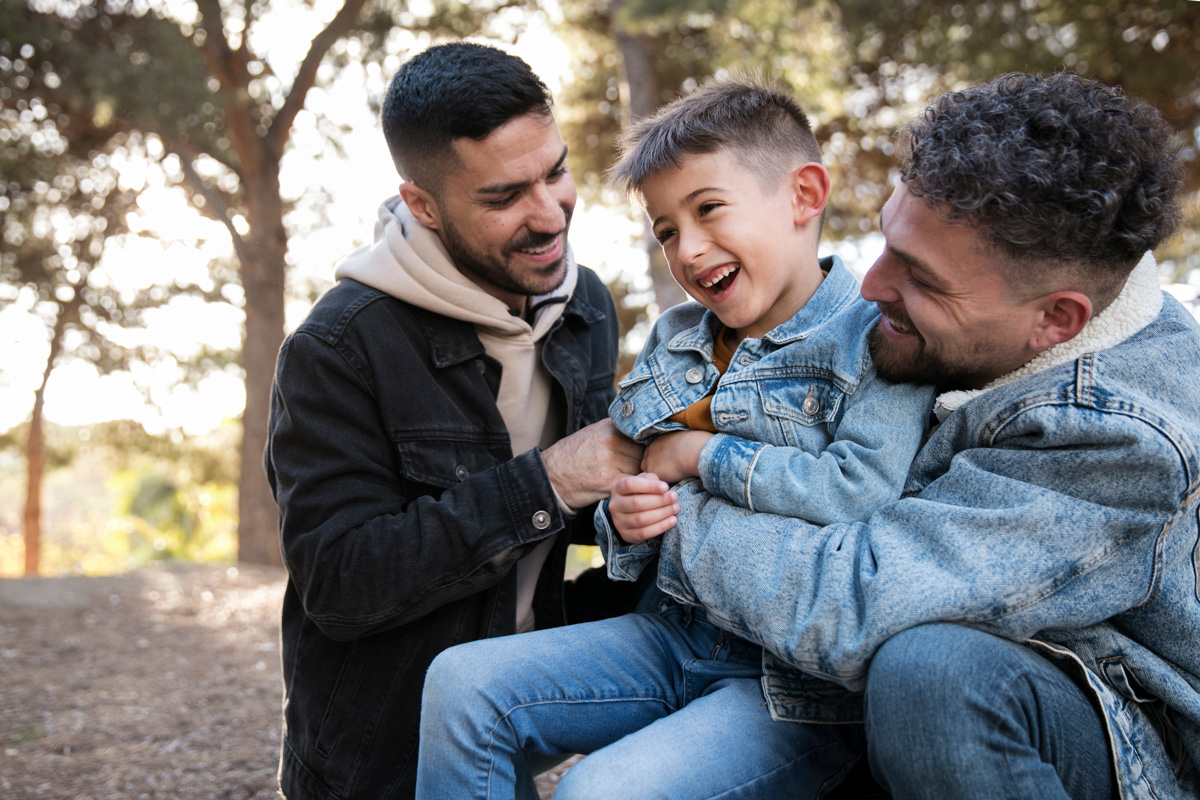 Two men are smiling while holding their child. See how Therapy for teens in MA can provide the parental support you need as anxious parents in Arlington, MA. Speak with a therapist today to learn more!