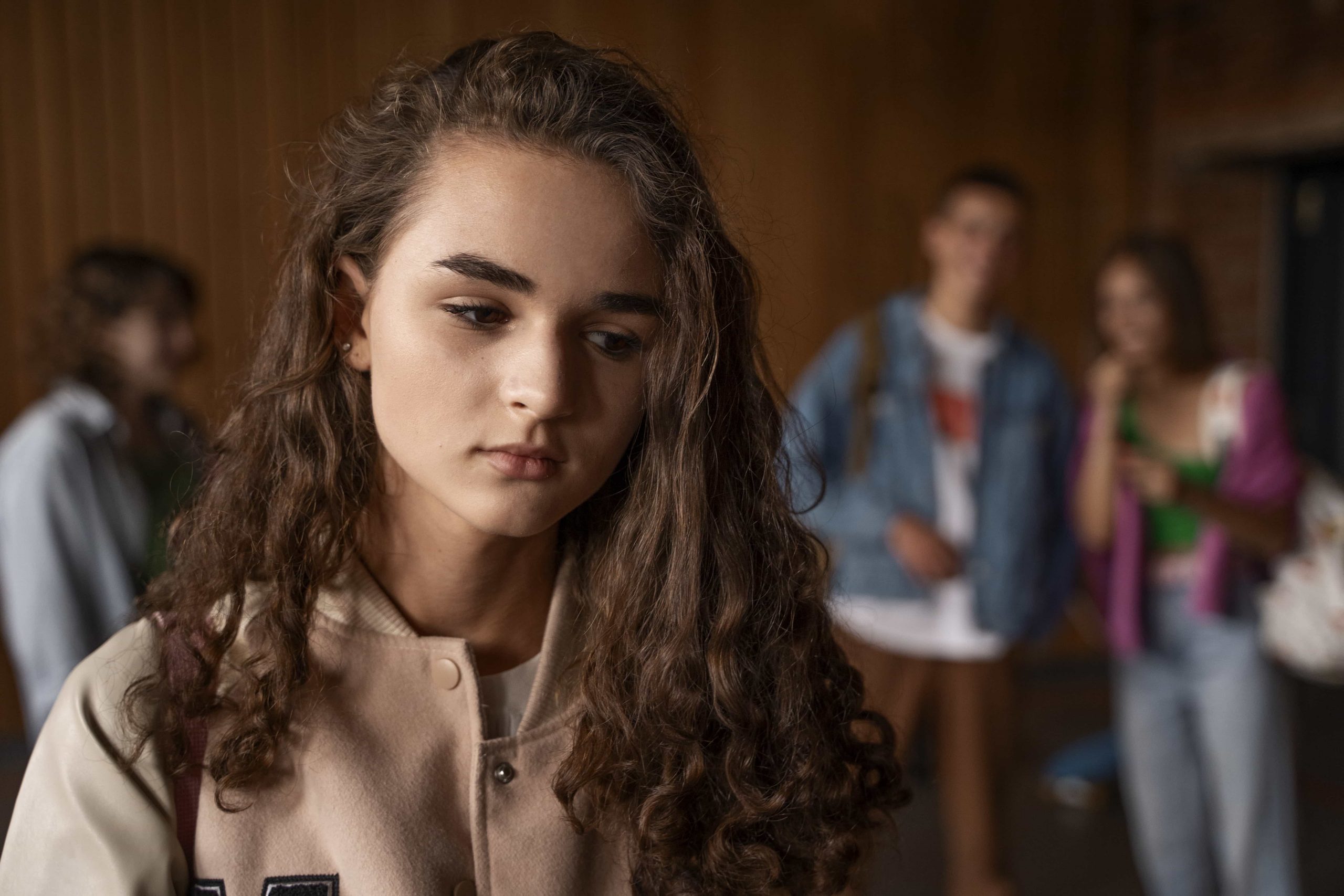A sad teen girl stands away from a group of teens. Does your teen need help? Speak with a teen therapist to see how Therapy for Teens in Arlington, MA can get them the help they need.