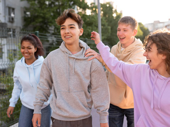 A teen boy stands around smiling with his teen friends in a group. Curious about what Acceptance and Commitment Therapy for Teens in Arlington, MA is? A teen therapist in MA can help answer those questions while helping your teen.