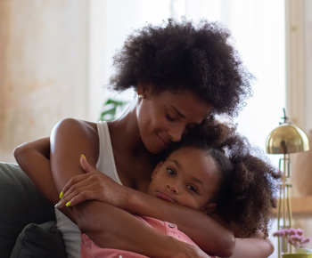 A teen daughter sits on her mothers lap to be comforted. Want to know how to help your teen navigate their emotions? Speak with a teen therapist to see how therapy for teens in Arlington, MA can help you and them.