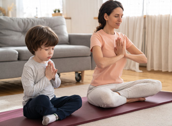 A woman sits on her floor doing yoga with her son. Struggling as Anxious Parents in Arlington, MA? Get Parenting Support through Therapy for Teens in Arlington, MA today!