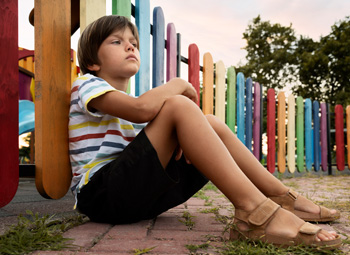 A boy sits against a fence looking sad, showing anxious body language. Learn how anxiety therapy in Arlington, MA can offer support by contacting a child therapist in Arlington, MA or searching for “child psychologist arlington, ma”.