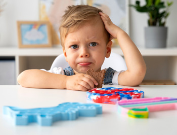 Little boy looking confused with toys in front of him. Learn how therapy for ADHD in Arlington, MA can offer support for children by searching for child counseling in Arlington, MA. Search for ADHD in Arlington, MA to learn more.