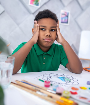 A child sits with head in hands while struggling with ADHD. This could represent the support a child therapist in Arlington, MA can offer via therapy for ADHD in Arlington, MA. Search for ADHD in Arlington, MA for more info.