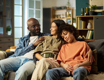 Two parents sit with their teen as they smile on a couch. This could represent the support family can offer for overcoming teen depression in Arlington, MA. Search for therapy for depression in Arlington, MA by searching for teen therapy in Arlington, MA today.