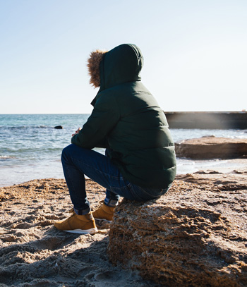 A teen sits alone while looking out over a shoreline. This could symbolize the loneliness that depression treatment in Arlington, MA can help teens overcome. Learn more about therapy for depression in Arlington, MA and how a teen counselor in Arlington, MA can help today.