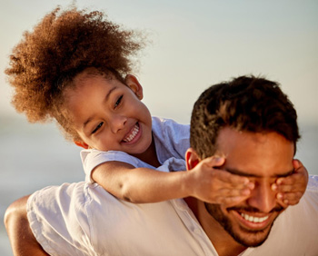 A close up of a parent playing with their child on a beach as the child smiles. This could represent overcoming symptoms of depression treatment in Arlington, MA. Search for a Child psychologist Arlington, MA and how telehealth in Alrington, MA can offer support today.