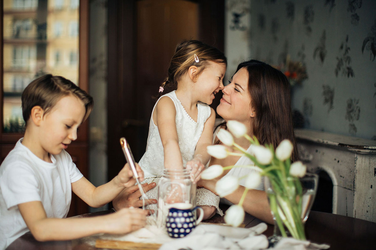 a mother smiles at her daughter while her son makes cookies