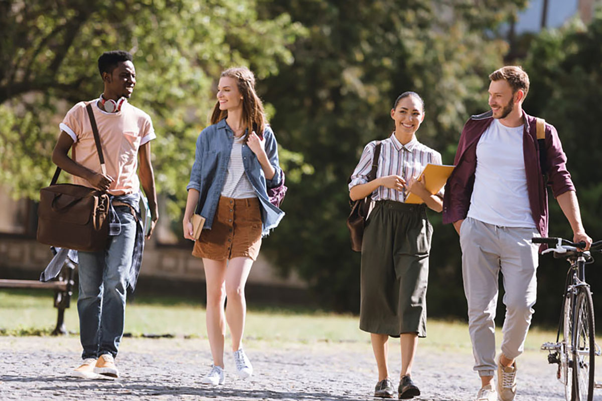 four diverse college students walk in a row on campus